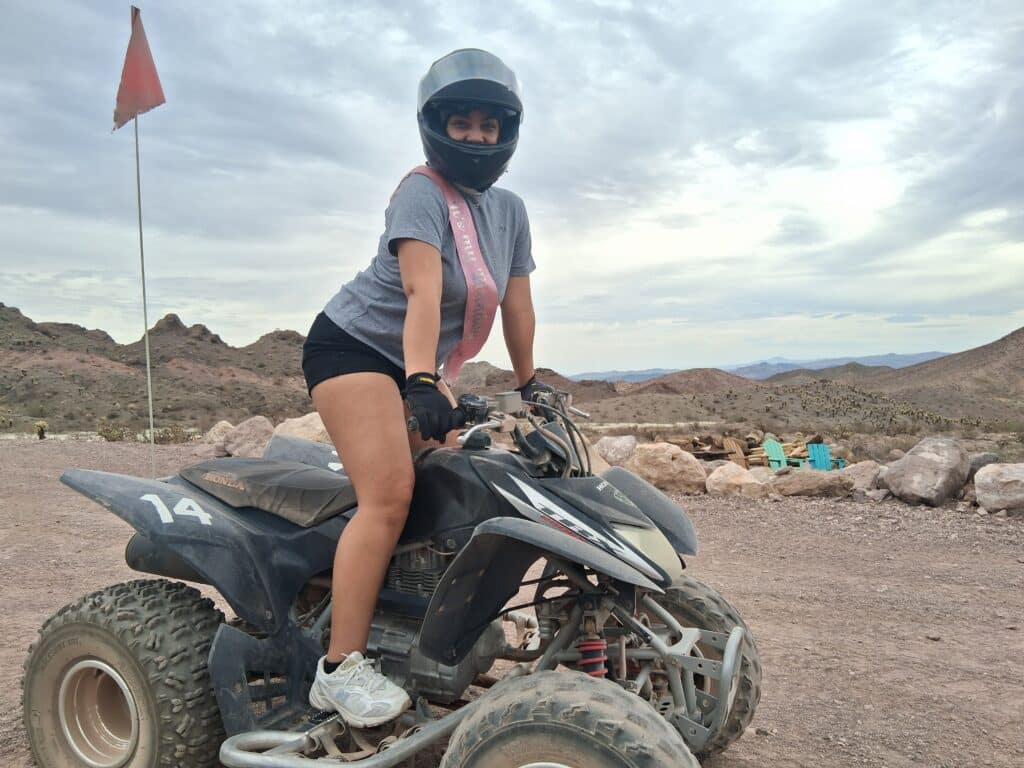 Smiling rider on a black ATV #14 enjoys a Las Vegas desert tour near Nevada mountains under cloudy skies.