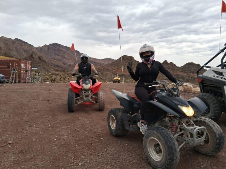 ATV tour near Las Vegas: two riders in helmets explore rocky Nevada trails with orange flags, mountains, and desert views.