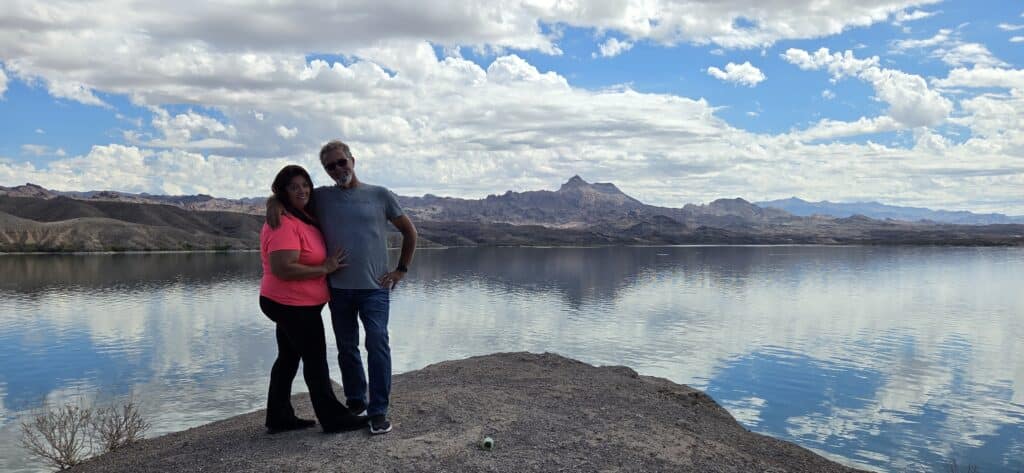 Couple on rocky Nevada lake shore near Colorado River, mountains behind; perfect for RZR rides or Las Vegas ATV adventure.