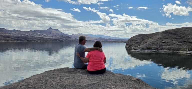 A couple sits on rocky Nevada shore by the Colorado River near Las Vegas, admiring mountains and planning ATV or RZR rides.