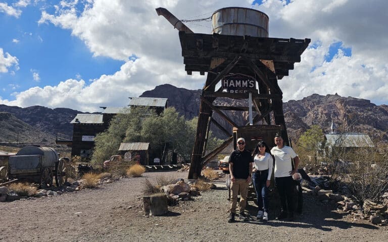 Smiling trio near Hamm’s Beer water tower at Nevada ghost town by Colorado River—perfect for Las Vegas ATV tours & sightseeing.
