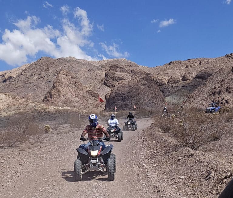 ATV riders explore a rocky desert trail near Las Vegas, Nevada, with brown mountains and blue sky—ideal for guided RZR off-road tours.