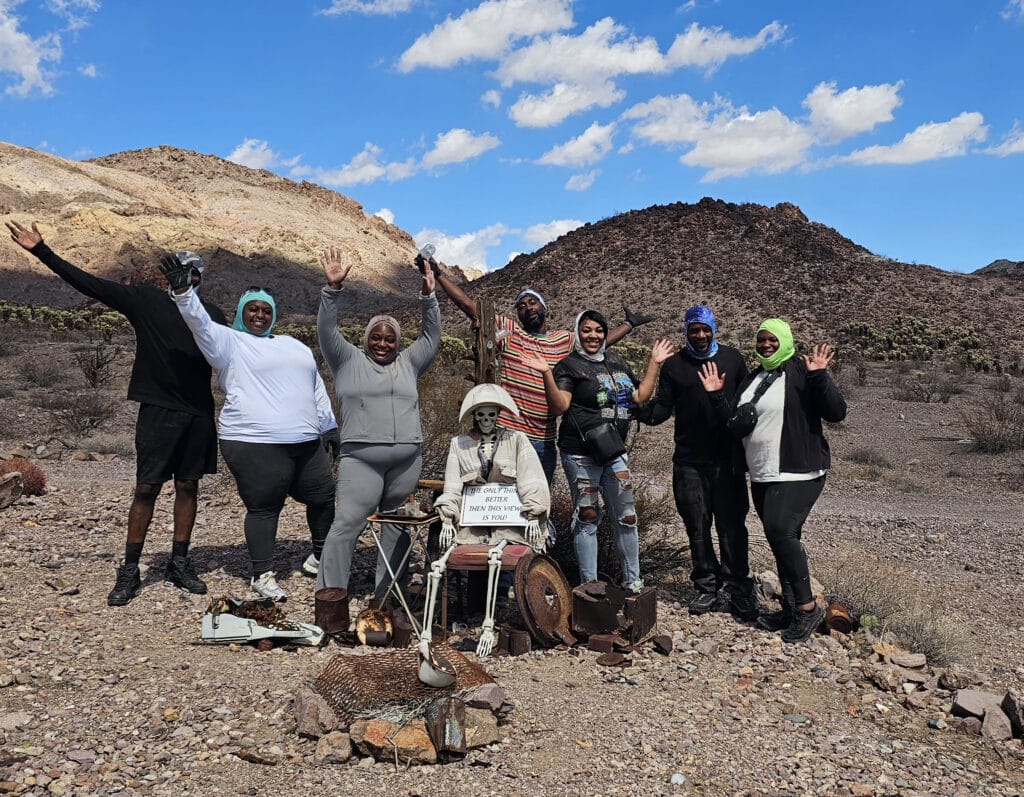Group waves in Nevada desert near rocky hills and skeleton with a “Thank you for visiting” sign—perfect for Las Vegas Ghost Town tours.