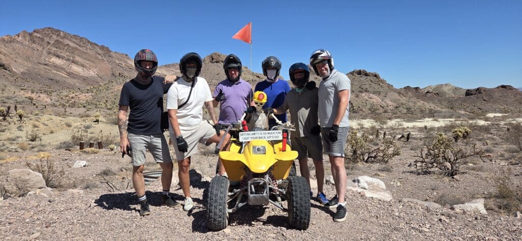 Group with helmets poses by yellow ATV in Nevada desert near Las Vegas, perfect for ATV tours and RZR off-road adventure rides.