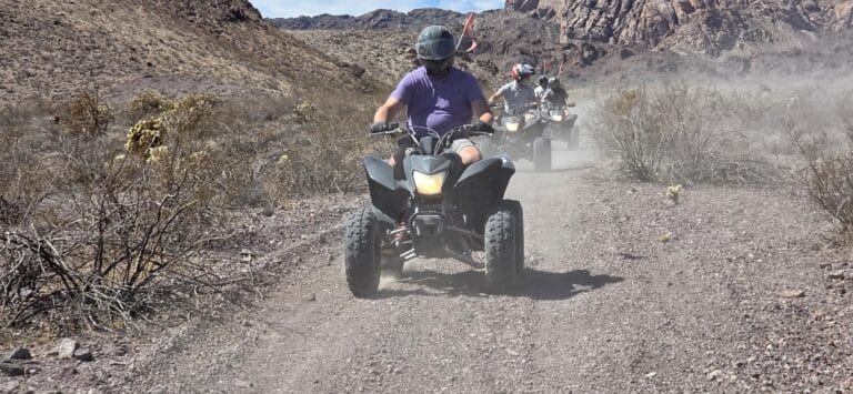 ATV riders explore a dusty Nevada desert trail near Las Vegas, with mountains and shrubs, on an exciting RZR off-road tour.