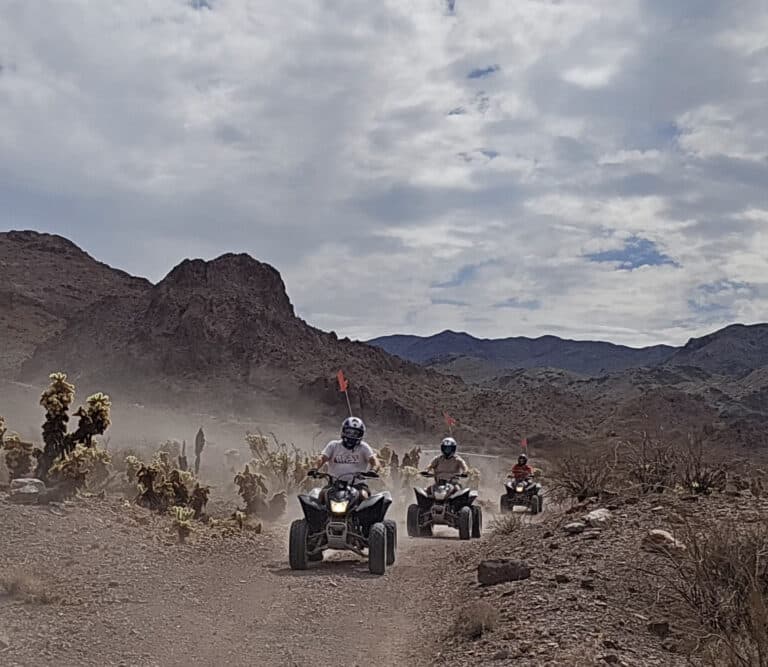 ATV riders explore a dusty Nevada desert trail near Las Vegas, rocky hills and cacti, on an exciting off-road tour adventure.