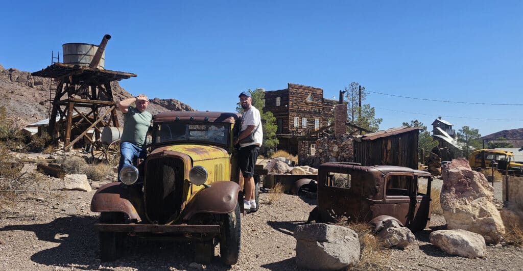 Two men by a vintage yellow car in a Nevada ghost town near Las Vegas, perfect for ATV tours and ghost town sightseeing.