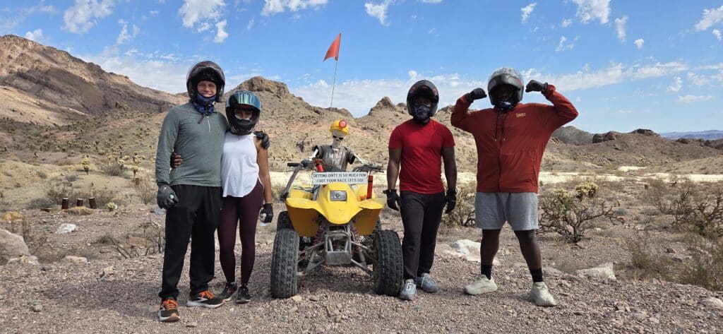Group in helmets and casual wear poses by yellow ATV in Nevada desert near Las Vegas, ready for an exciting ATV tour adventure.