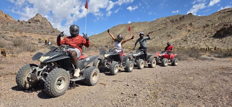 Group on ATVs raises arms in Nevada desert near Las Vegas, enjoying an exciting ATV tour under blue skies.