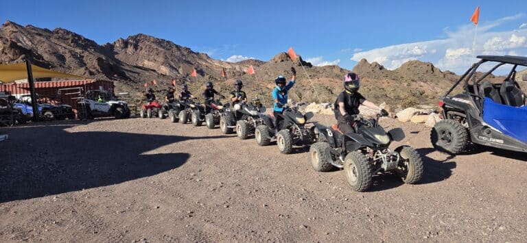 Riders in helmets sit on ATVs ready for a Nevada desert trail near Las Vegas, with RZR tours and mountain views.