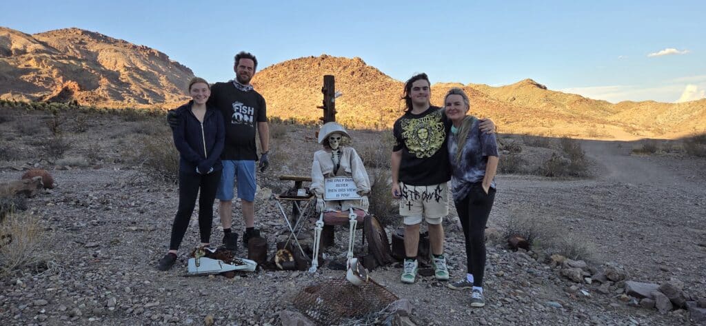 Group poses by skeleton at a quirky table in Nevada desert near Las Vegas, perfect for Ghost Town sightseeing at sunset.