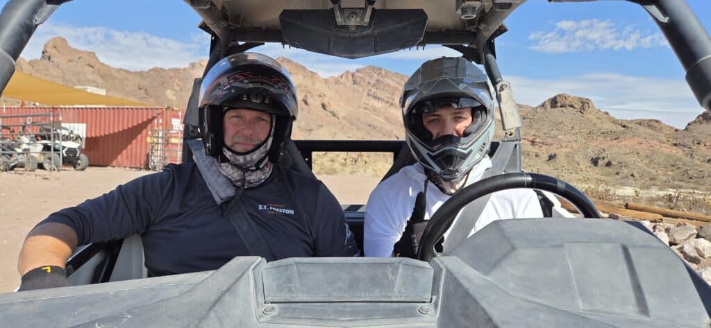 Two people in helmets sit inside an RZR for an ATV tour near Las Vegas, Nevada, with rocky desert and mountains in the background.