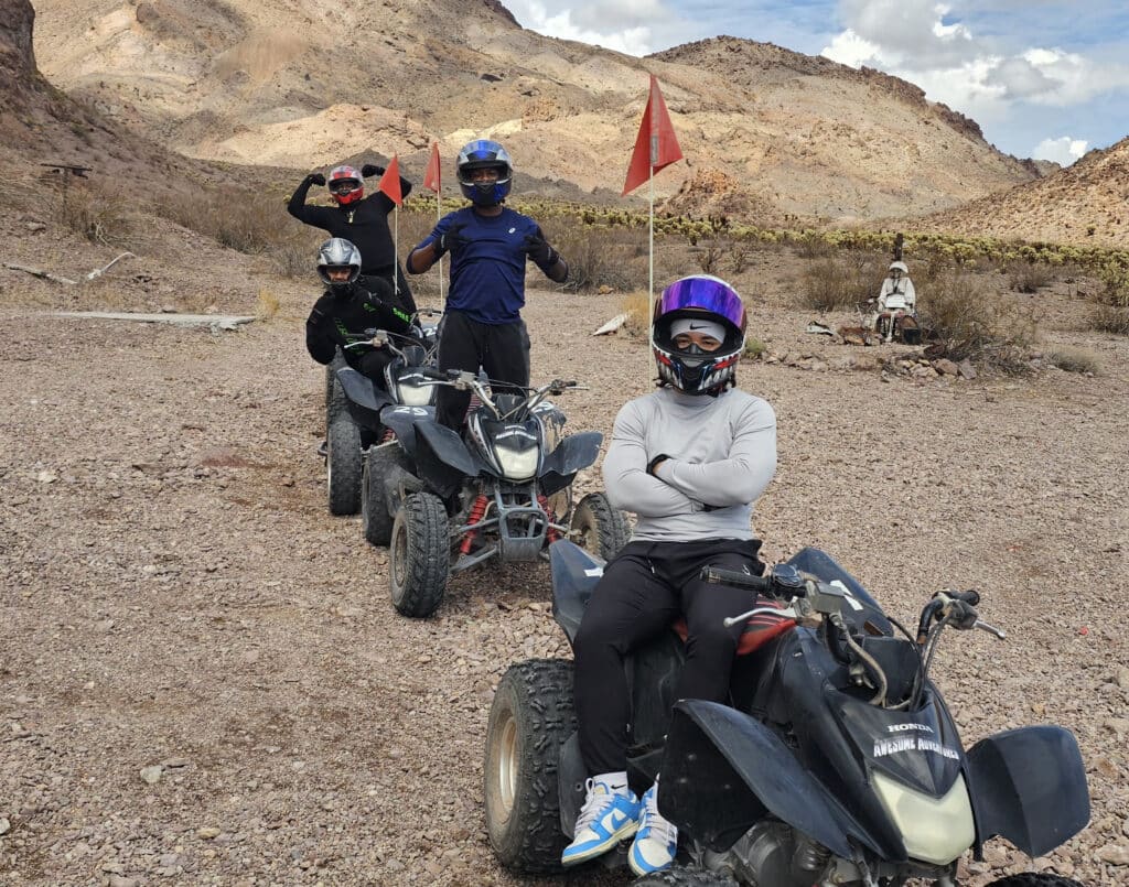 Group on black ATVs with red flags in Nevada’s rocky desert near Las Vegas, ready for an exciting ATV tour adventure.