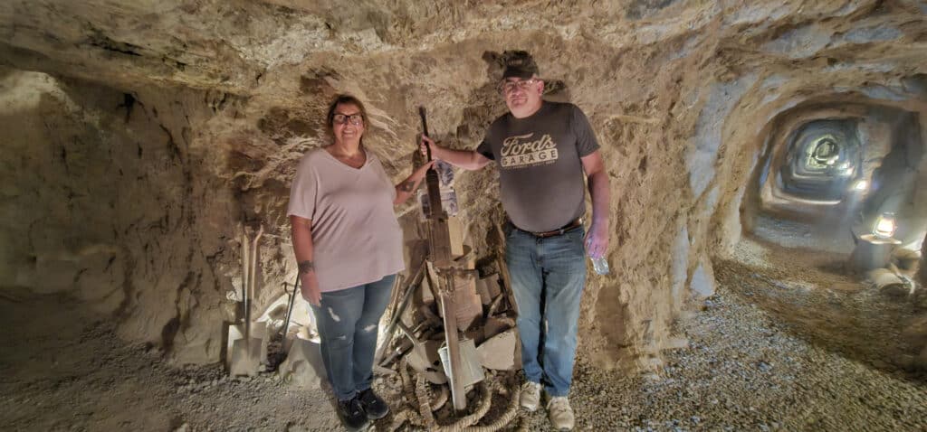 Two visitors pose in a dim Nevada mining tunnel near Las Vegas, with headlamps and tools—perfect for Ghost Town sightseeing tours.