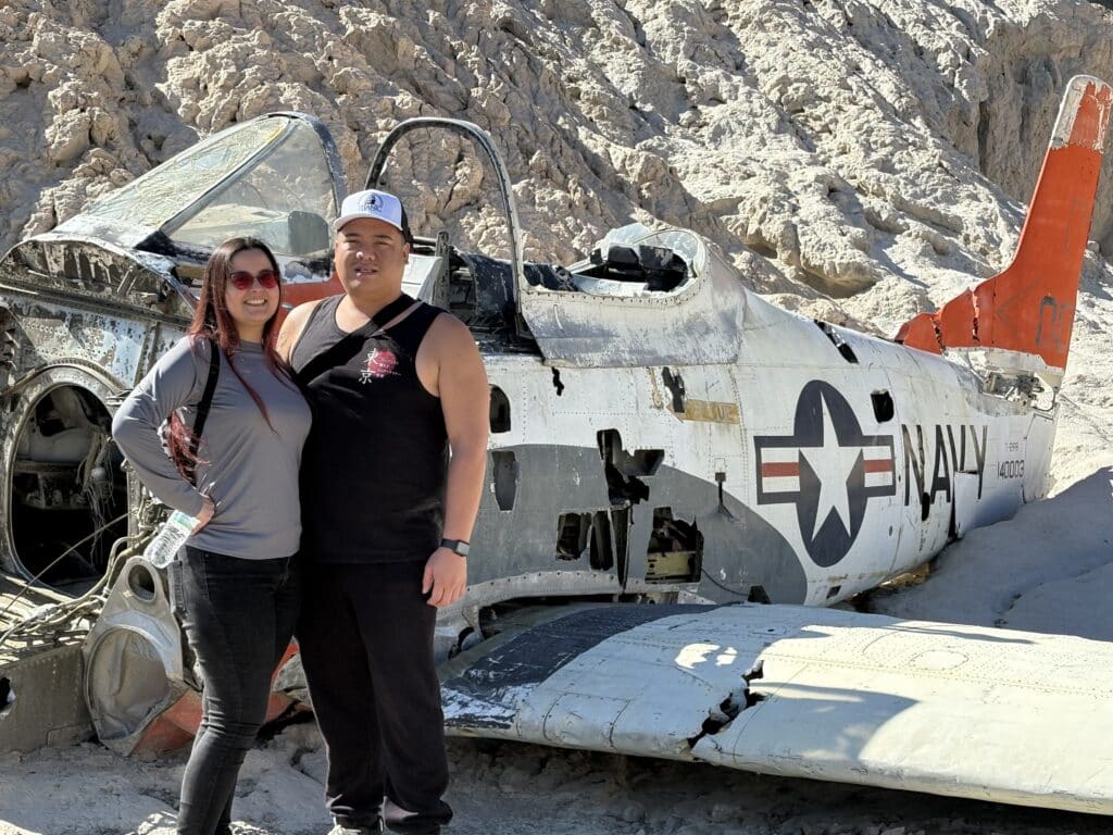 Smiling couple at a crashed U.S. Navy plane near Las Vegas, Nevada—perfect for ATV tours and Ghost Town sightseeing adventures.