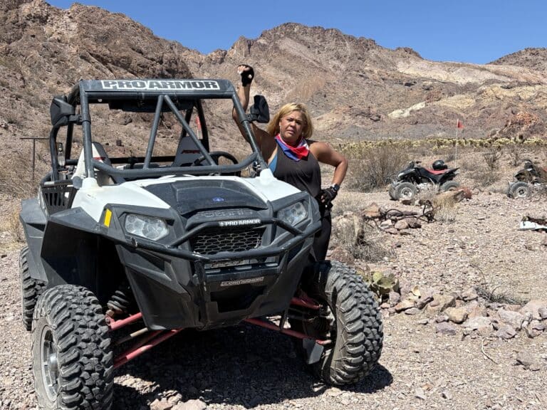 Woman with bandana poses by white ATV during a Nevada desert RZR tour near Las Vegas, mountains and other ATVs visible.