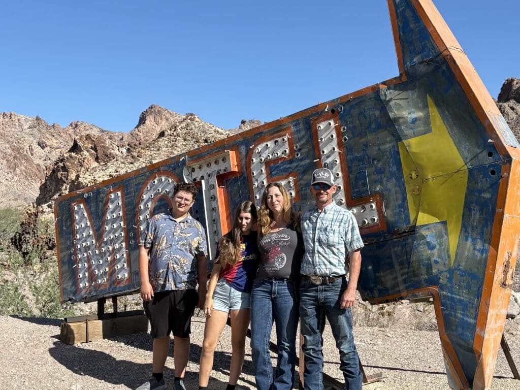 Smiling friends pose by a vintage MOTEL sign near rocky Nevada hills, perfect for Las Vegas ATV tours and Colorado River sightseeing.