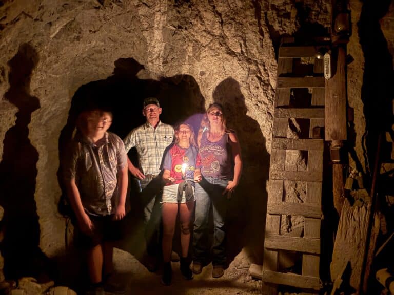 Adventurers with flashlights explore a dim cave near the Colorado River, Nevada, with ladder access after ATV tours from Las Vegas.