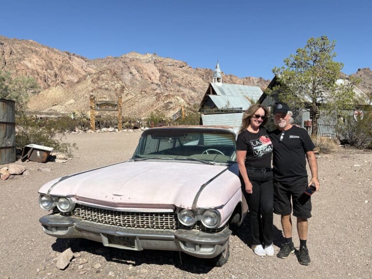 A smiling couple poses by a vintage pink car in a Nevada desert near Las Vegas, perfect for Ghost Town sightseeing and ATV tours.