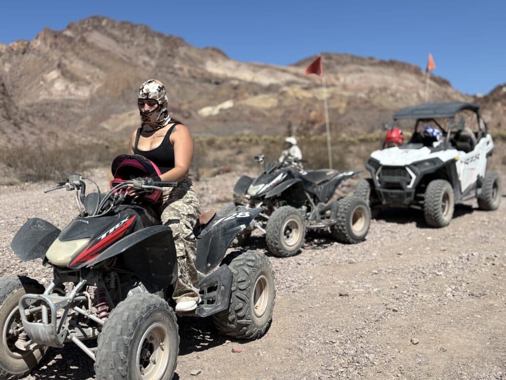 Riders on an ATV tour near Las Vegas speed along a rocky desert trail with mountains and blue sky in scenic Nevada.