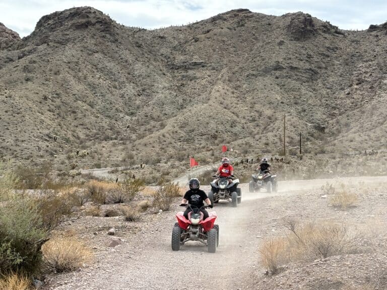 Riders on ATVs explore a dusty Nevada desert trail near Las Vegas, with rocky hills—ideal for ATV tours and off-road adventures.