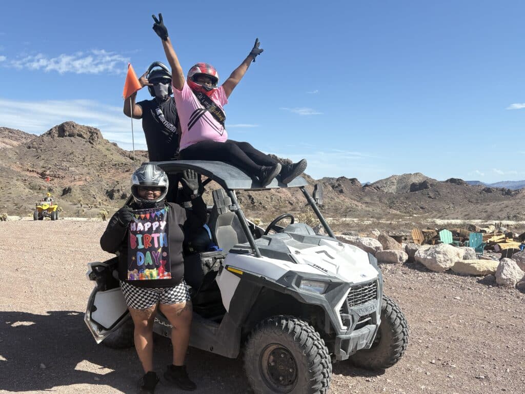 Three people on an ATV tour near Las Vegas pose in helmets with mountains behind, celebrating Nevada off-road adventure.