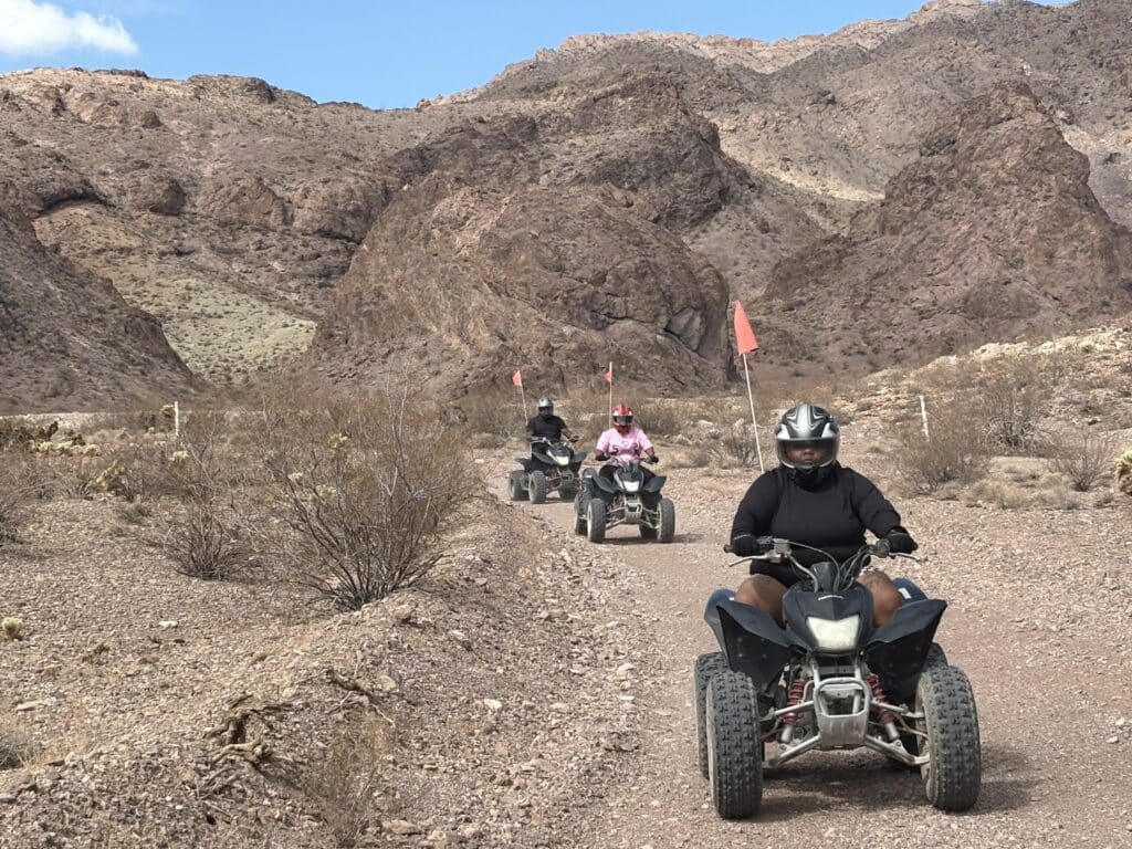 Adventurers on ATVs explore a rocky Nevada trail near Las Vegas under a partly cloudy sky, perfect for thrilling ATV tours.