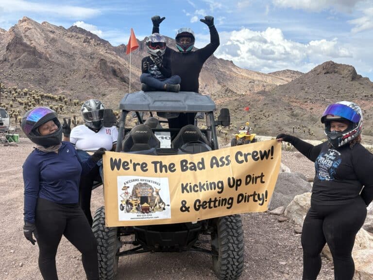 Adventure-seekers in helmets pose with a “Bad Ass Crew” banner on RZR during an ATV tour near the Colorado River, Nevada desert.