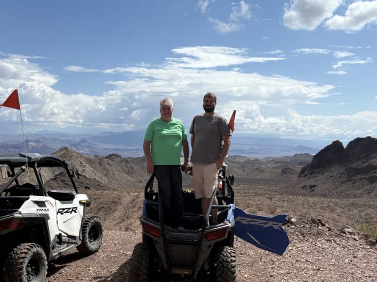 Adventure seekers stand on an ATV in Nevada’s desert near Las Vegas; RZR off-road tours by Colorado River, rugged mountains behind.