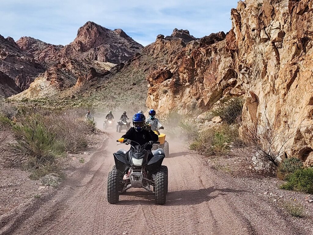 Adventurers on ATVs ride dusty Nevada trails near Las Vegas, with rocky cliffs—top ATV tour to Colorado River or Ghost Town.