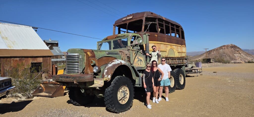 Four people pose by a vintage military truck in a Nevada desert ghost town near Las Vegas, perfect for sightseeing tours.