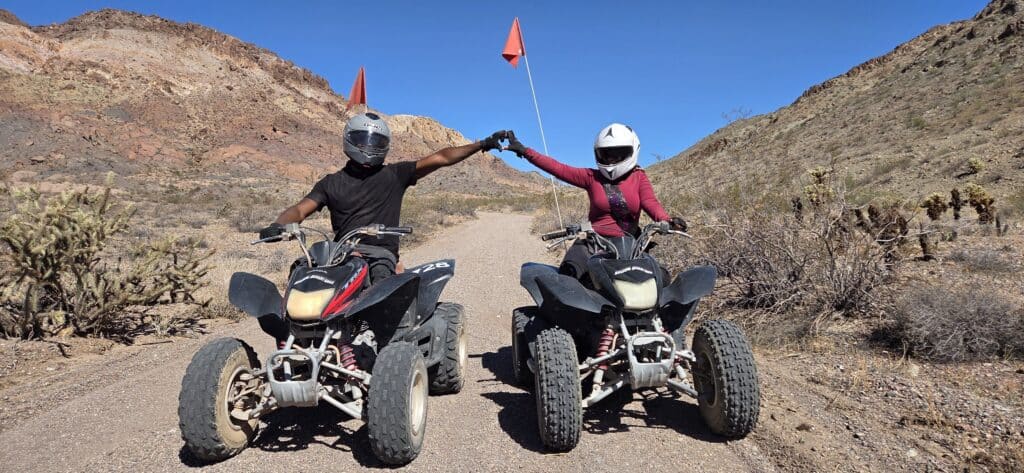 ATV riders in Nevada near Las Vegas fist bump on a desert trail, orange flags waving. Perfect for thrilling ATV tours and RZR rides.