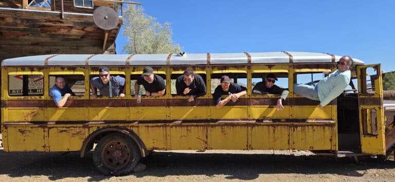 Seven men lean from a vintage yellow bus in a Nevada ghost town—perfect for Las Vegas ATV tours and desert sightseeing.