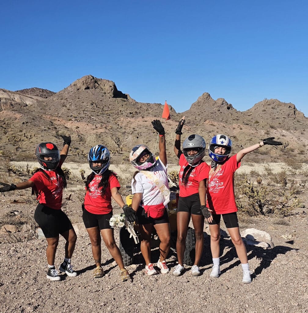 Group in red shirts and helmets poses on Nevada rocky terrain near Las Vegas, ready for an ATV tour under clear blue skies.