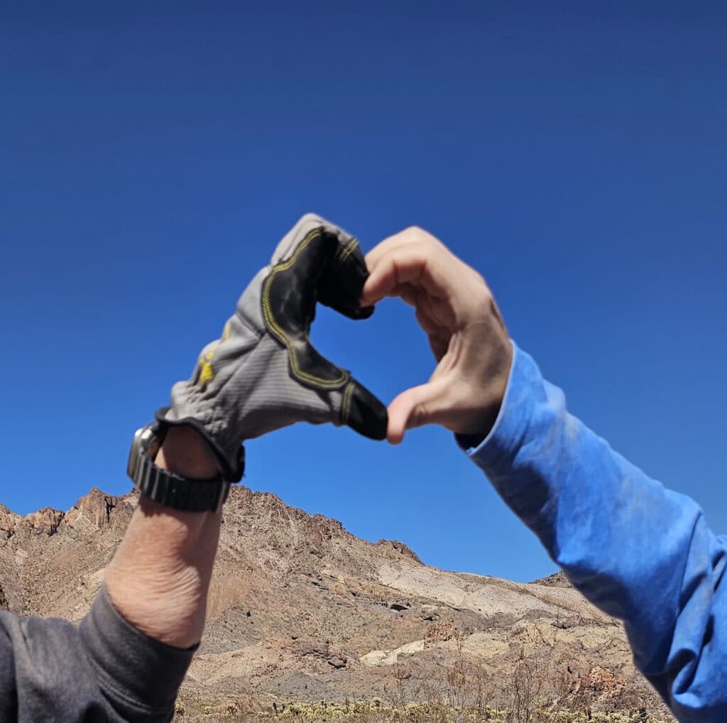 Hands form a heart with a blue sky and Nevada desert mountains near the Colorado River—perfect for Las Vegas ATV or RZR tours.