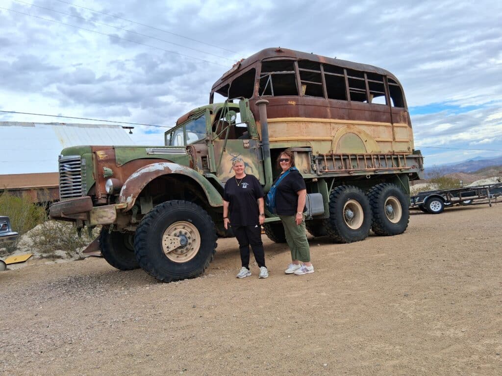 Two women smile in front of a rusty military truck at a Nevada ghost town, perfect for Las Vegas ATV tours and sightseeing.