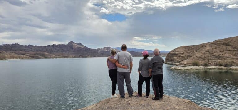 Group on a rocky Nevada shore gazes at Colorado River lake, perfect for Las Vegas ATV tours or RZR off-road adventures.