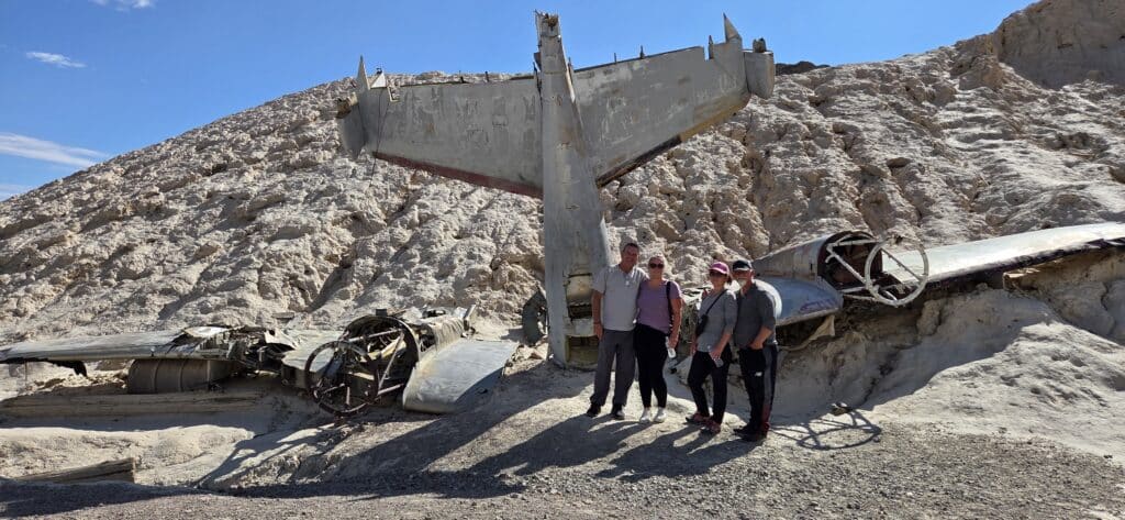 Four people by a crashed airplane in Nevada desert near Las Vegas, ideal for ATV tours or Ghost Town sightseeing under blue skies.