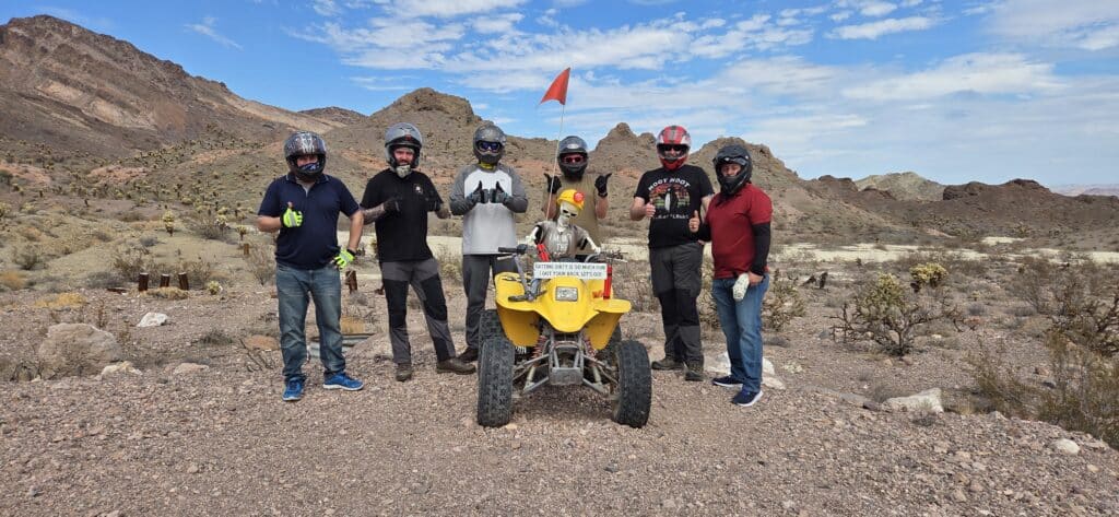 Group in helmets and gloves poses by a yellow ATV in Nevada desert near Las Vegas, ready for an exciting ATV tour adventure.