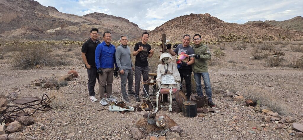 Seven men relax by a dressed skeleton in Nevada desert near Las Vegas, perfect for RZR rides or Ghost Town sightseeing adventures.
