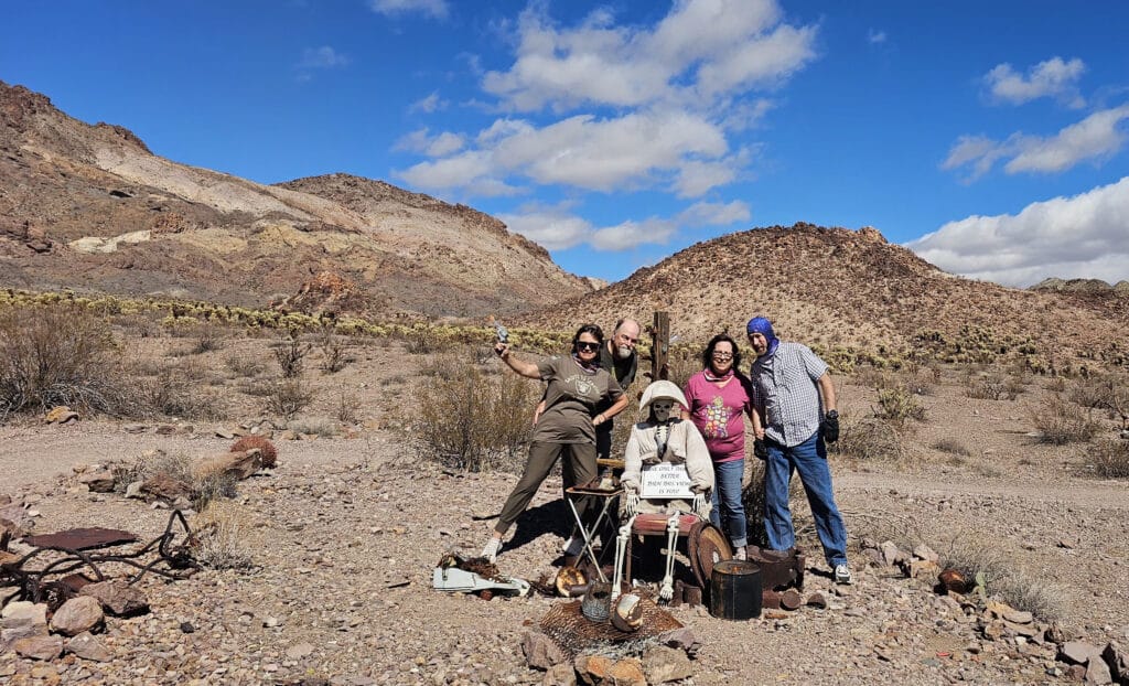 Smiling group in a rocky Nevada desert near Las Vegas, posing by a ghost town figure—ideal for ATV tours or sightseeing.