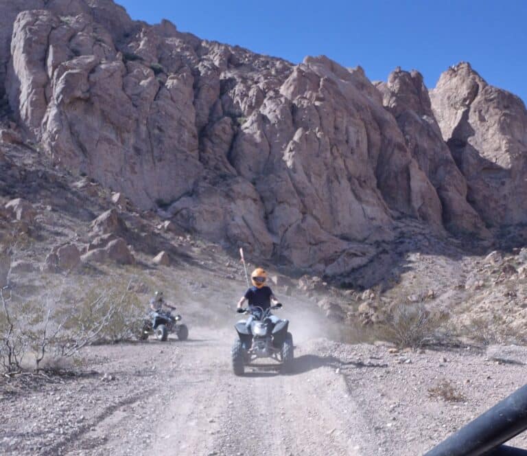 Adventurers enjoy an ATV tour on a dusty Nevada trail near Las Vegas, with rocky mountains and desert scenery under a clear sky.