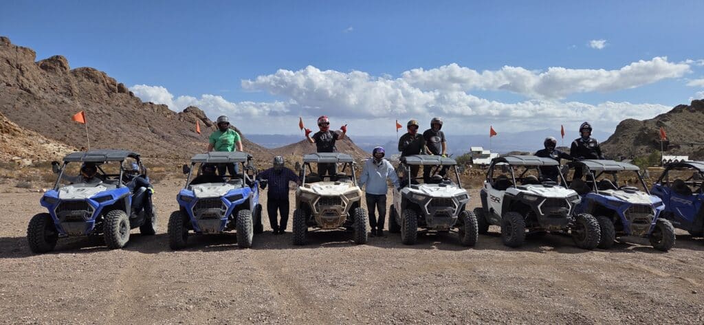 Group enjoys an ATV tour near Las Vegas, posing with RZRs in Nevada’s desert, rocky hills and gear-clad adventurers visible.