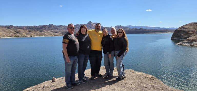 Group smiles on rocky ledge above Colorado River near Las Vegas, Nevada, with mountains behind—perfect for RZR ATV or Ghost Town tours.