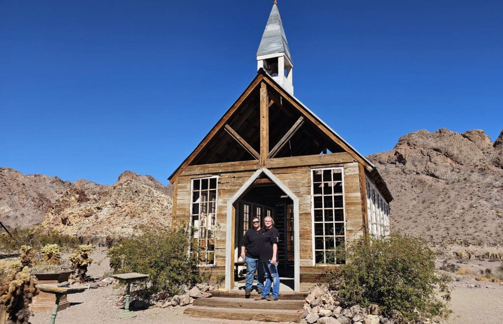 Two people at a rustic wooden church in a Nevada desert near Las Vegas, perfect for Ghost Town sightseeing and ATV tours.