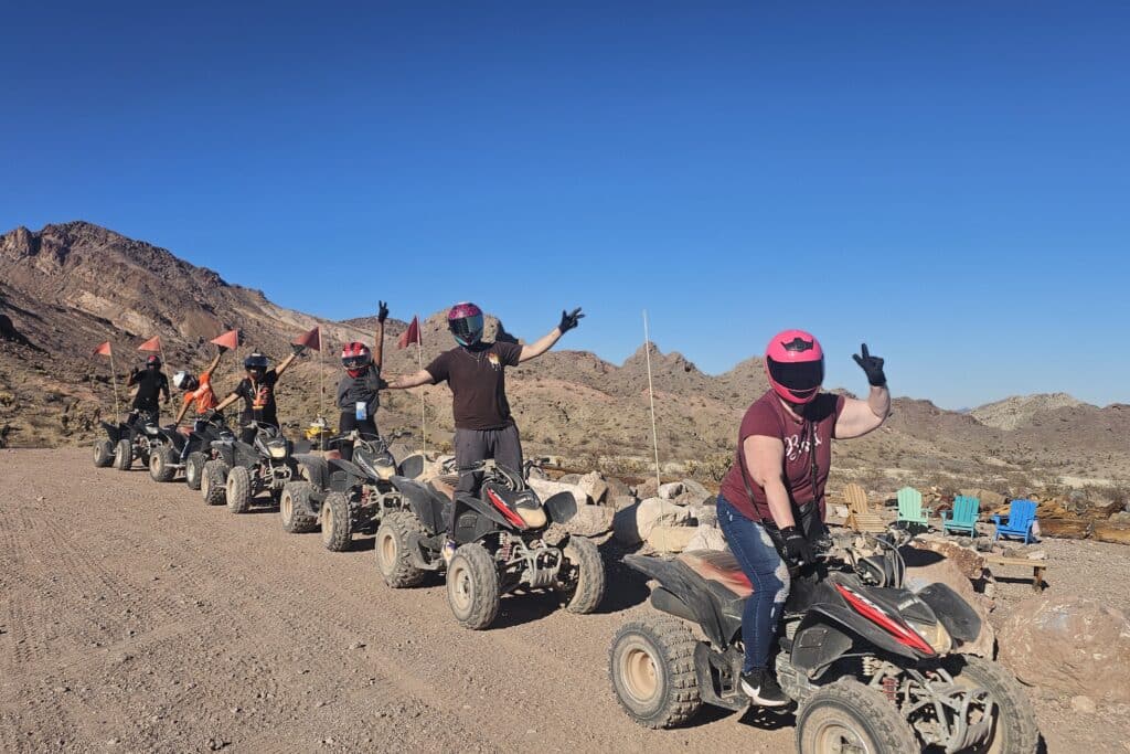 Group on ATVs enjoy a Nevada desert trail near Las Vegas, posing with peace signs during an exciting ATV tour under clear blue skies.