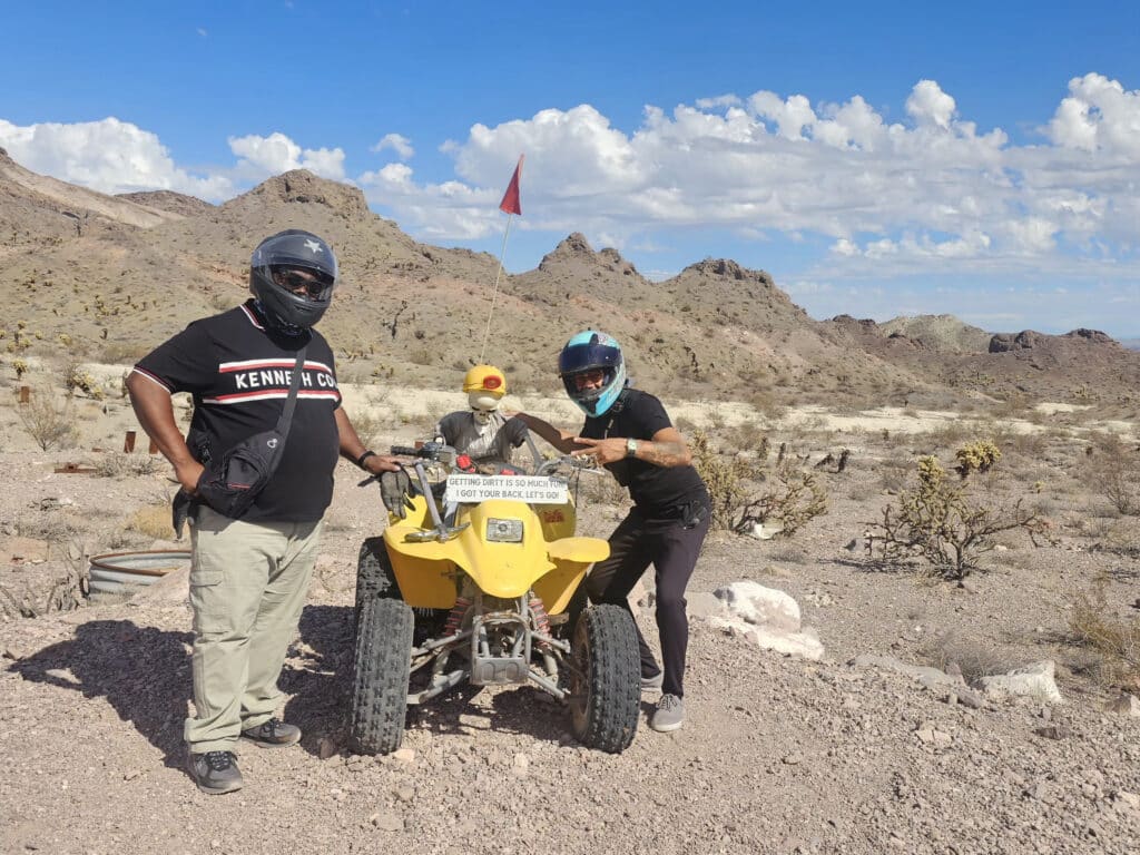 Two people in helmets with a yellow ATV near Nevada mountains, enjoying an exciting Las Vegas desert ATV tour adventure.