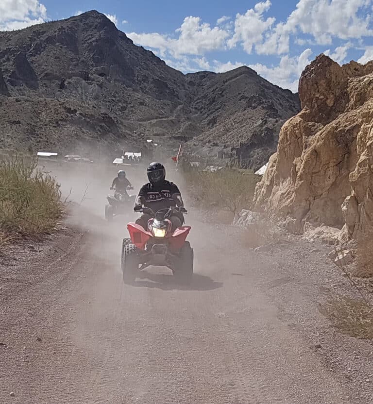 ATV riders speed along a dusty Nevada desert trail near Las Vegas, mountains in view, enjoying an exciting off-road ATV tour.
