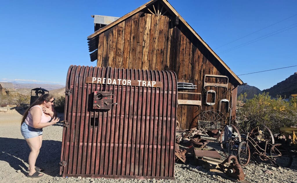 Woman peers into Predator Trap near rustic building in a Nevada ghost town, perfect for Las Vegas off-road and ATV tour adventures.
