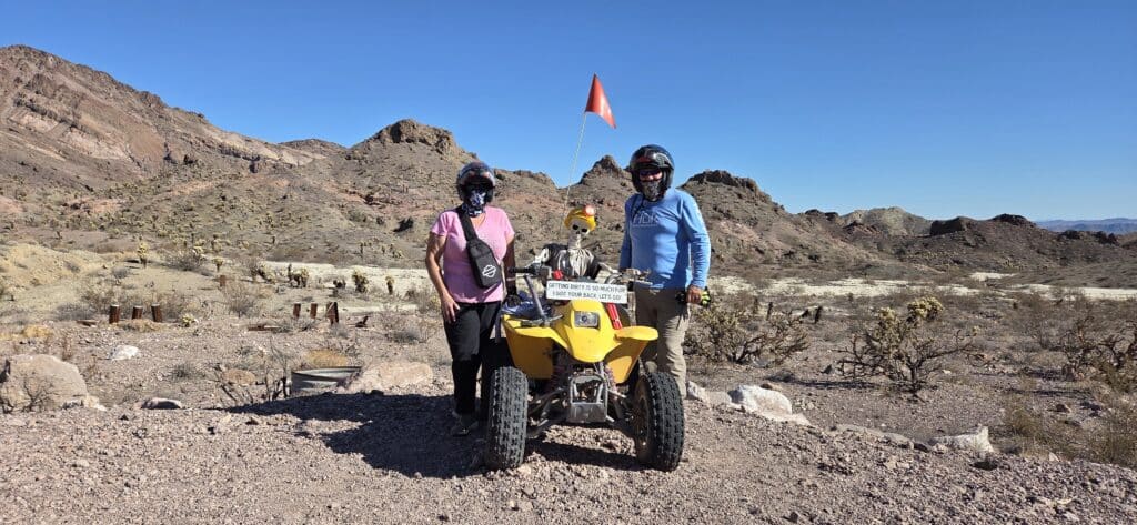 Adventure in Nevada: Two people in helmets with a dog on a yellow ATV, ready for off-road RZR tour near Las Vegas desert mountains.